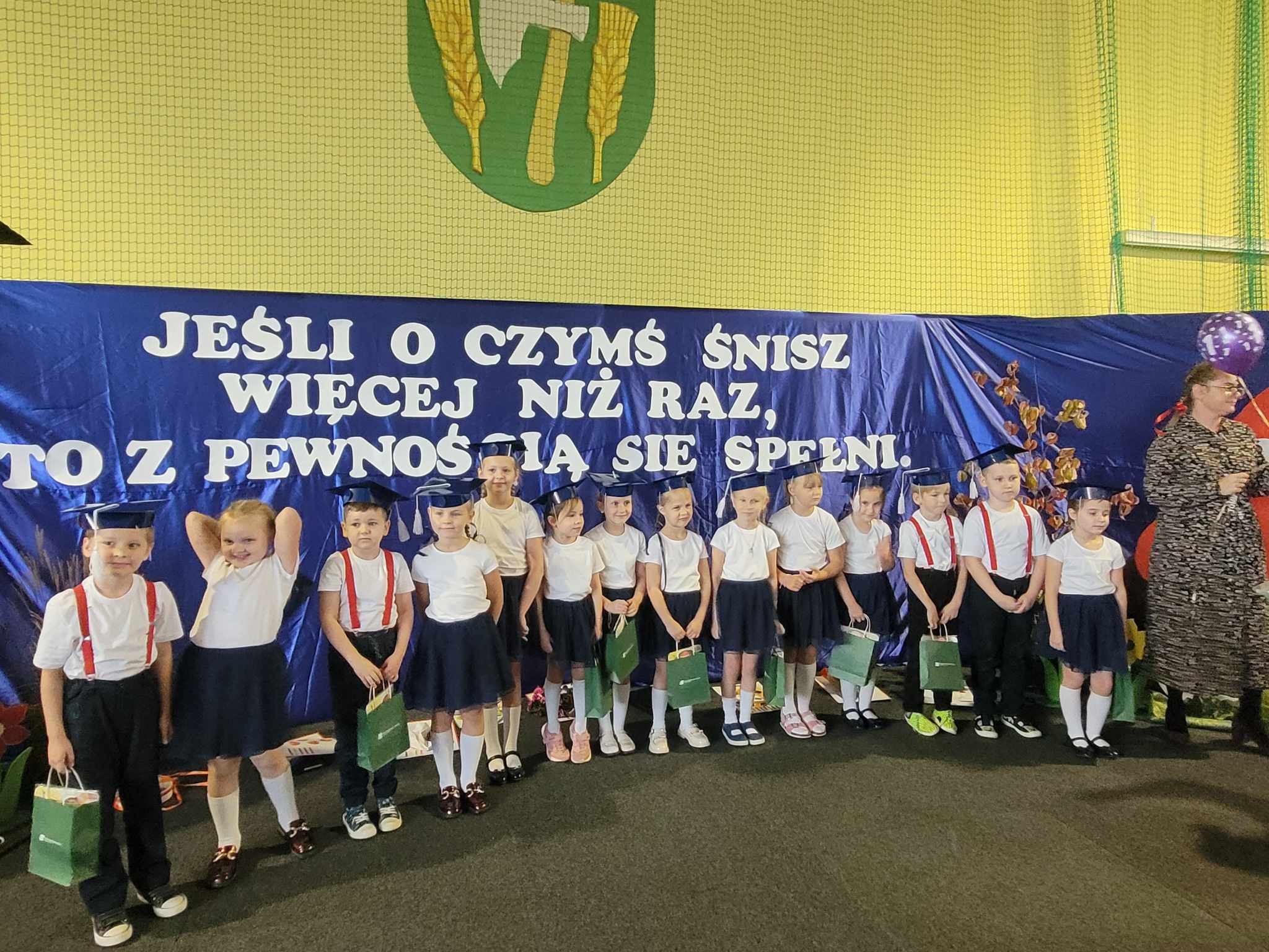 Uczniowie z upominkami na tle napisu: Jeśli o czymś śnisz...