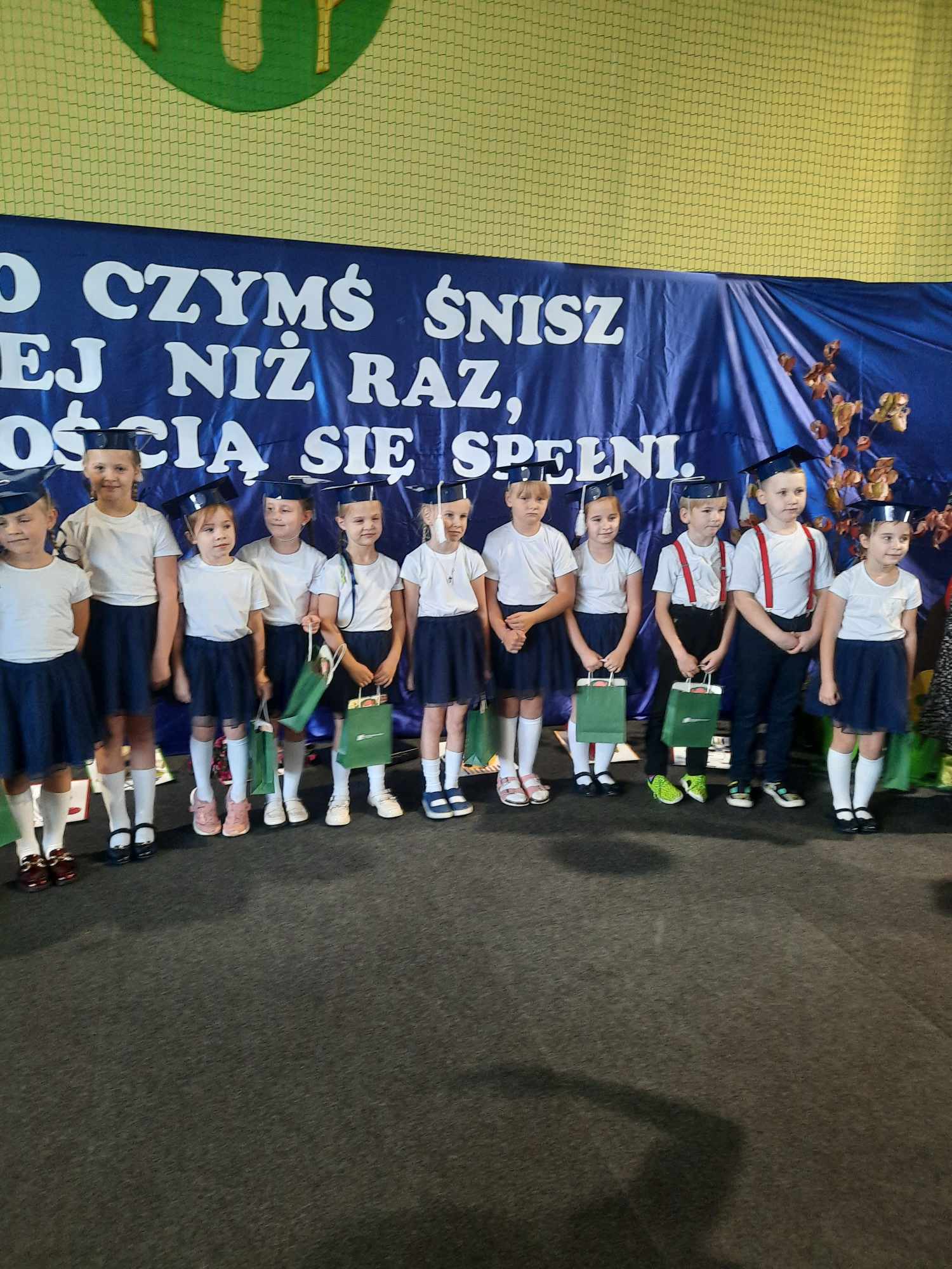 Grupa dzieci z zielonymi torbami na tle napisu motywacyjnego