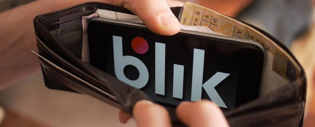 Telefon z logo BLIK wsunięty do portfela między dokumenty i banknoty