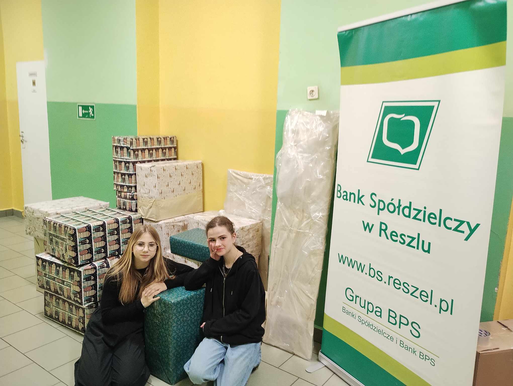 Dwie dziewczyny przy paczkach i banerze Banku Spółdzielczego w Reszlu
