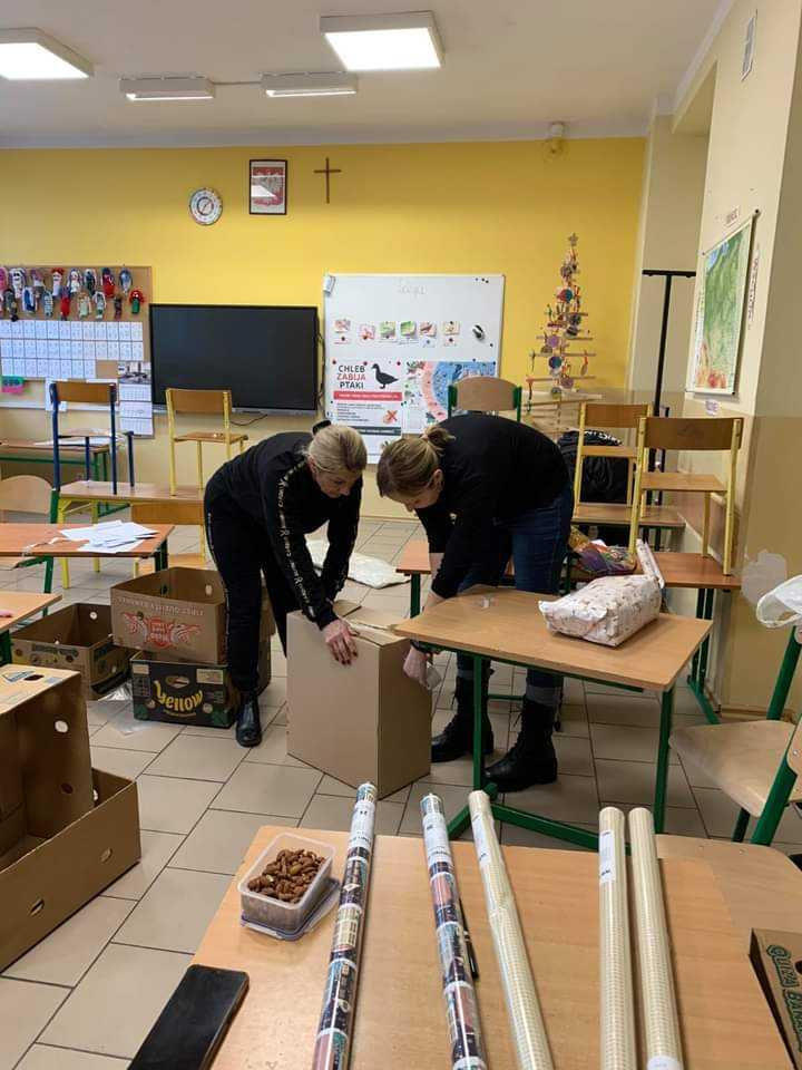 Dwie kobiety przygotowują paczki w szkolnej sali z ozdobami
